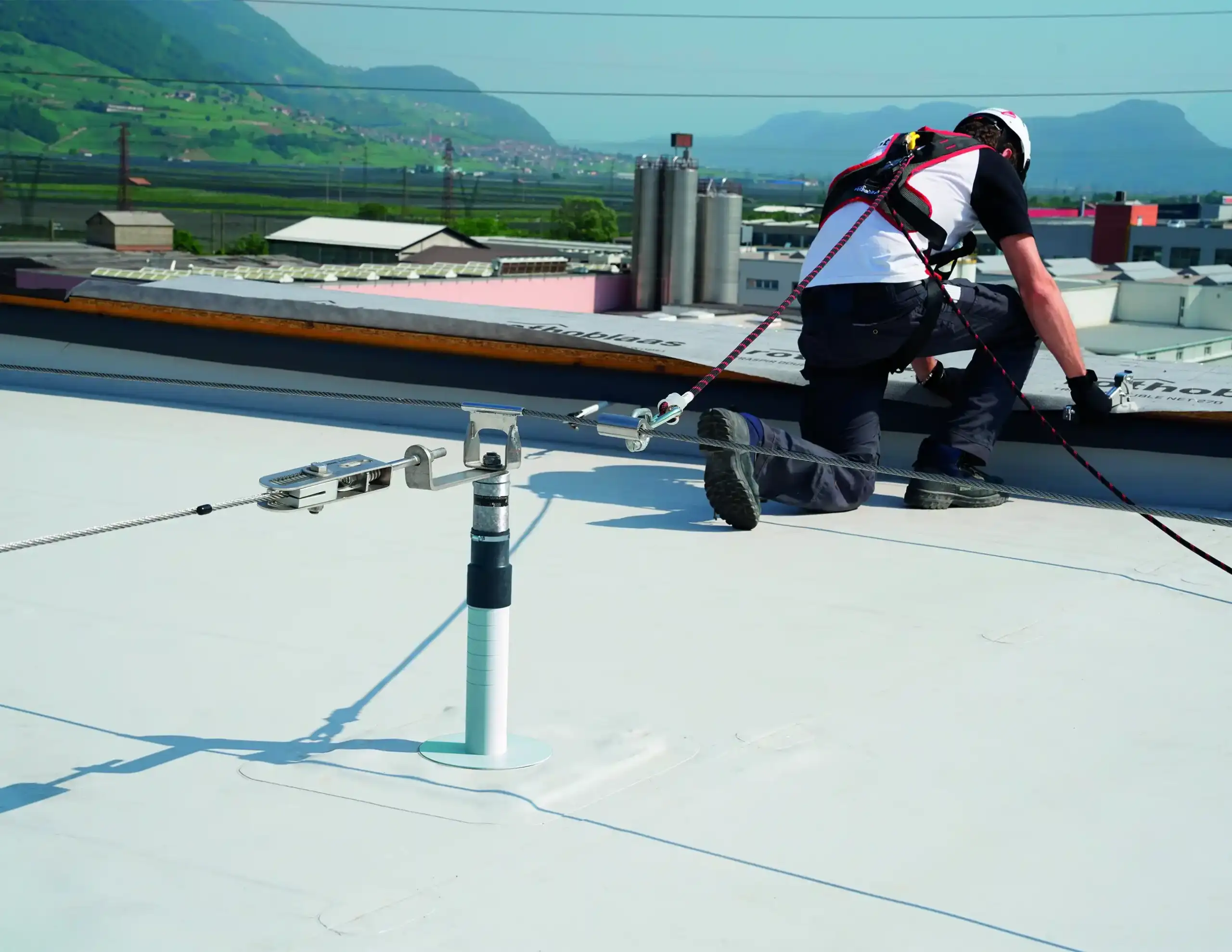 Foto di un installatore di un pannello fotovoltaico sopra un tetto agganciato ad un palo con una corda di sicurezza di Rothoblass